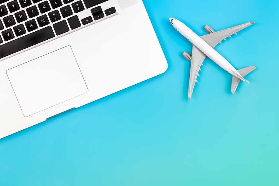 Laptop and airplane miniature on blue background, flat lay, copy space.